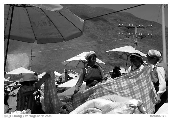 Bai women examining a piece of cloth at the Monday market. Shaping, Yunnan, China (black and white)