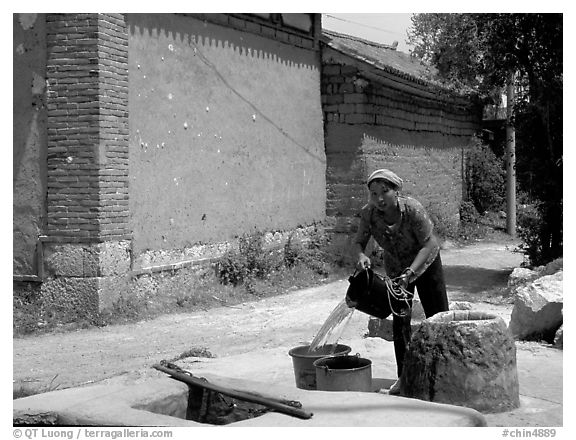 Bai woman fills up a water bucket at the well. Shaping, Yunnan, China (black and white)