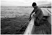 Cormorant fisherman catches one of his birds to retrieve the fish it caught. Dali, Yunnan, China ( black and white)