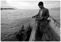 Cormorant fisherman feeds small fish to his birds as a prize for catching large fish. Dali, Yunnan, China (black and white)