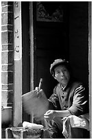 Naxi woman at doorway selling broiled corn. Lijiang, Yunnan, China (black and white)