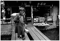 Naxi woman peddling eggs  to local residents walks acros a canal. Lijiang, Yunnan, China (black and white)