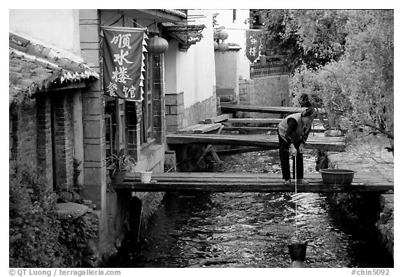 Woman fills up a water buck in the canal. Lijiang, Yunnan, China (black and white)