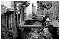 Woman fills up a water buck in the canal. Lijiang, Yunnan, China (black and white)