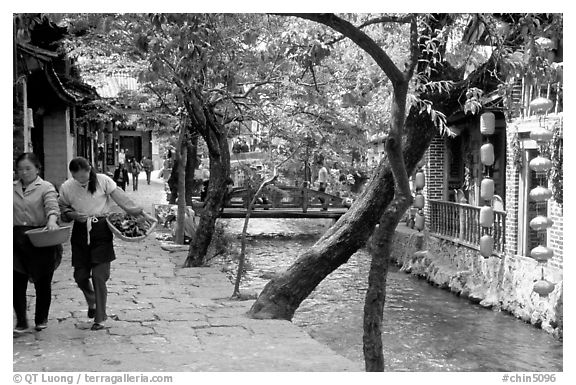 Naxi women walk along a canal. Lijiang, Yunnan, China (black and white)