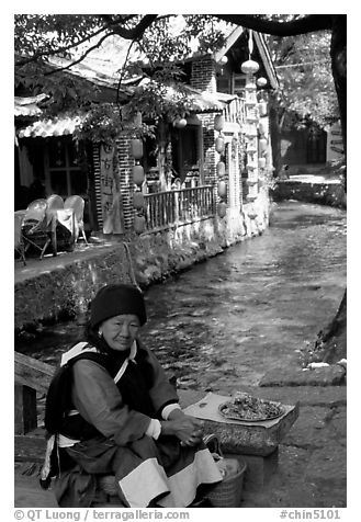 Elderly naxi woman peddles candies near a canal. Lijiang, Yunnan, China