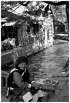 Elderly naxi woman peddles candies near a canal. Lijiang, Yunnan, China ( black and white)