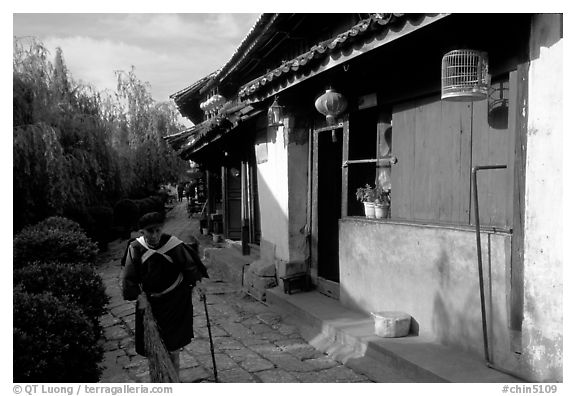 Naxi woman sweeps the floor at the door of her wooden house. Lijiang, Yunnan, China (black and white)