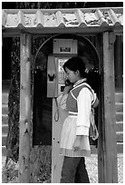 Woman in Naxi dress in a telephone booth. Lijiang, Yunnan, China (black and white)