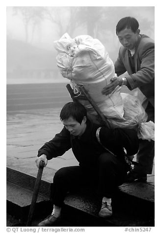 Porter getting helped to shoulder a heavy load on a back frame. Emei Shan, Sichuan, China (black and white)