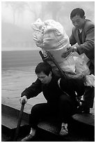 Porter getting helped to shoulder a heavy load on a back frame. Emei Shan, Sichuan, China (black and white)