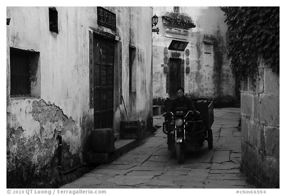 Man driving motobike carriage in narrow street. Xidi Village, Anhui, China (black and white)