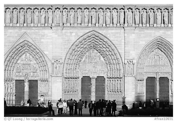 People and facade and gates of Notre Dame Cathedral, late afternoon. Paris, France (black and white)
