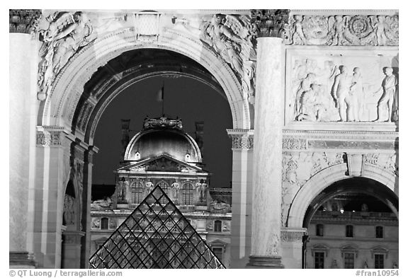 Louvre and  pyramid  seen through the Carousel triumphal arch at night. Paris, France