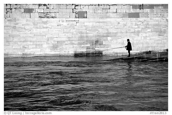 Man standing at water level fishing in the Seine River. Paris, France