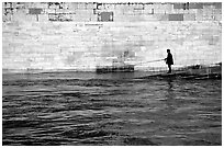 Man standing at water level fishing in the Seine River. Paris, France (black and white)