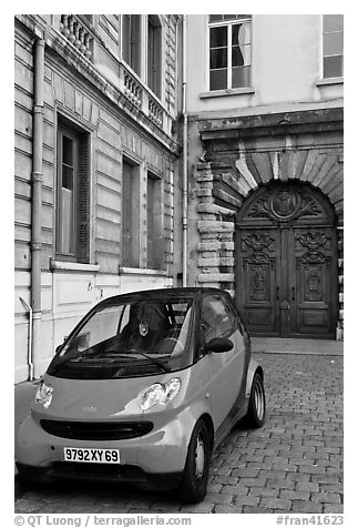 Tiny car on coblestone pavement in front of historic house. Lyon, France (black and white)