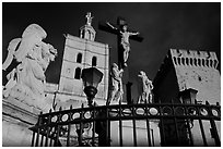 Cross with Christ, statues, and towers, evening light. Avignon, Provence, France (black and white)