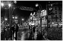 Metro entrance, boulevard, and Moulin Rouge on rainy night. Paris, France (black and white)