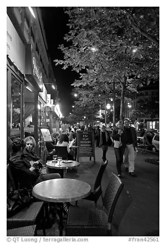 Couple walking by outdoor tables of cafe at night. Paris, France