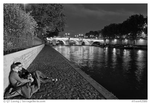 Couple sitting on quay on banks of the Seine River. Paris, France