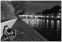 Couple sitting on quay on banks of the Seine River. Paris, France (black and white)