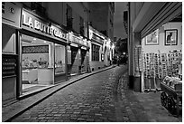 Narrow cobblestone street and businesses at night, Montmartre. Paris, France (black and white)