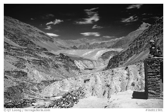 Woman sitting on roof of house in front of mountain landscape, Zanskar, Jammu and Kashmir. India (black and white)