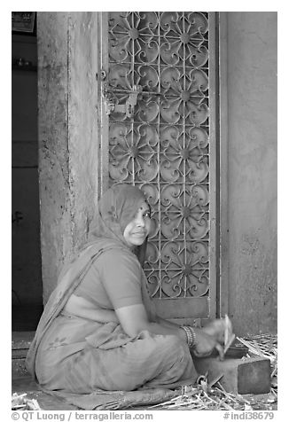 Woman in orange sari sitting next to green door and blue wall. Jodhpur, Rajasthan, India