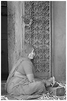 Woman in orange sari sitting next to green door and blue wall. Jodhpur, Rajasthan, India (black and white)