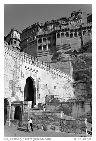 Couple walking below gate and high walls, Mehrangarh Fort. Jodhpur, Rajasthan, India (black and white)