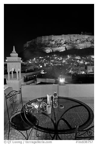 Rooftop restaurant table with food served and view of Mehrangarh Fort by night. Jodhpur, Rajasthan, India
