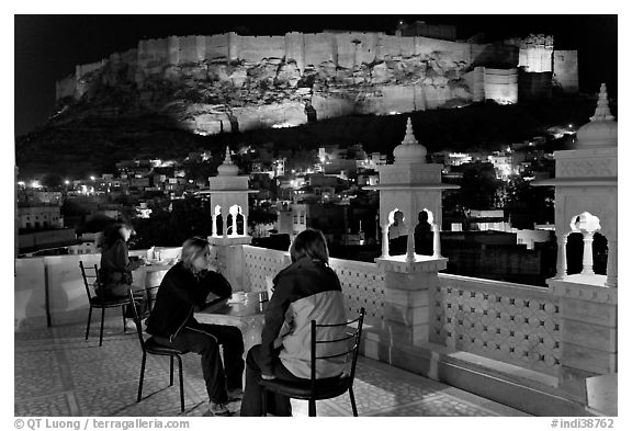 Travelers on rooftop terrace with view of Mehrangarh Fort by night. Jodhpur, Rajasthan, India (black and white)