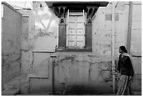 Woman walks infront of blue tinted whitewashed wall. Jodhpur, Rajasthan, India (black and white)