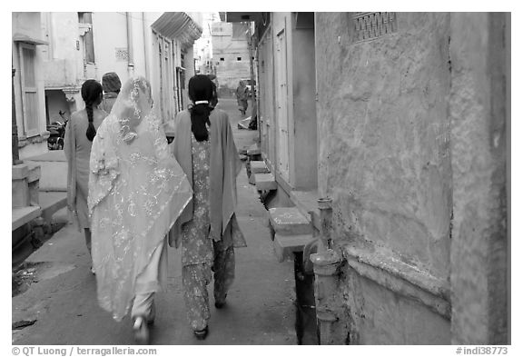 Women walking in narrow alley with blue walls. Jodhpur, Rajasthan, India (black and white)