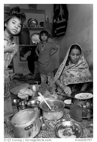 Woman cooking, flanked by two girls. Jodhpur, Rajasthan, India