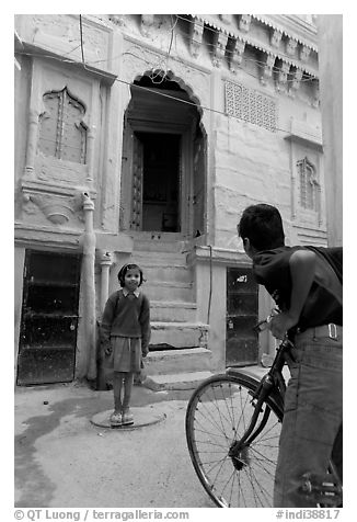 Boy on bicycle looking at girl in front of blue house. Jodhpur, Rajasthan, India (black and white)