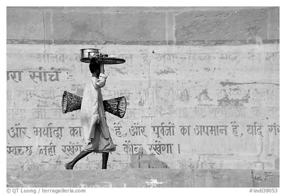 Man carrying a plater in front of wall with inscriptions in Hindi. Varanasi, Uttar Pradesh, India (black and white)