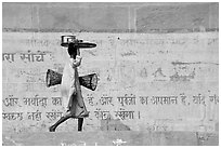 Man carrying a plater in front of wall with inscriptions in Hindi. Varanasi, Uttar Pradesh, India (black and white)