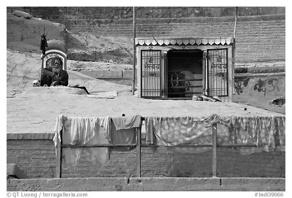 Sadhu sitting next to shrine and laundry. Varanasi, Uttar Pradesh, India (black and white)