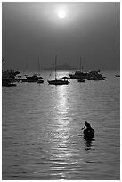 Man fishing from rowboat and anchored yachts, sunrise. Mumbai, Maharashtra, India (black and white)