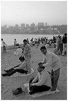 Head masseurs and Mumbai skyline at sunset,  Chowpatty Beach. Mumbai, Maharashtra, India (black and white)