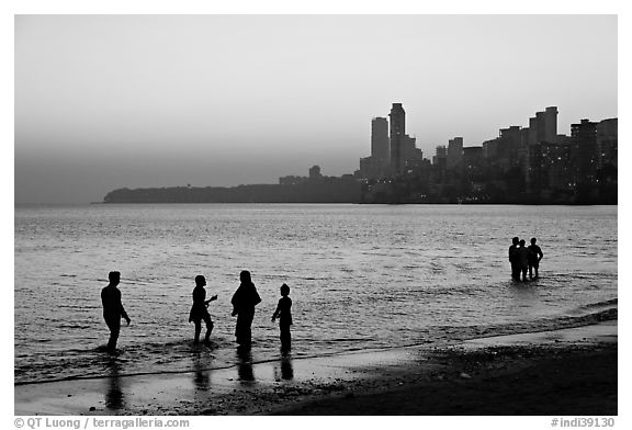 People standing in water at sunset with skyline behind, Chowpatty Beach. Mumbai, Maharashtra, India (black and white)