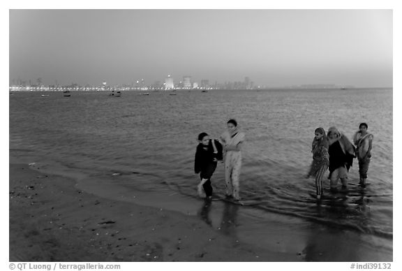 Women walking in water by night, Chowpatty Beach. Mumbai, Maharashtra, India (black and white)