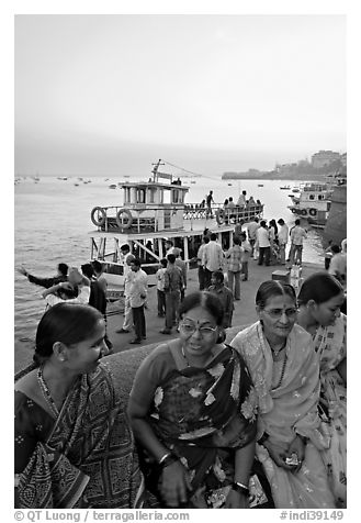 Women sitting on waterfront with boats behind at twilight. Mumbai, Maharashtra, India