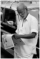 Man reading newspaper next to taxi. Mumbai, Maharashtra, India (black and white)