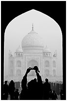 Tourist pointing  digital camera to Maj Mahal, framed by arch of gateway. Agra, Uttar Pradesh, India (black and white)