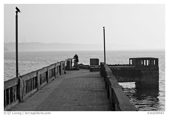 Pier with man fishing, early morning, Dona Paula. Goa, India (black and white)