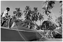 Men mending fishing net with palm trees in background. Goa, India (black and white)