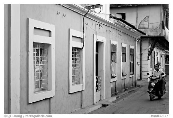 Men on motorbike driving through blue house, Panjim. Goa, India